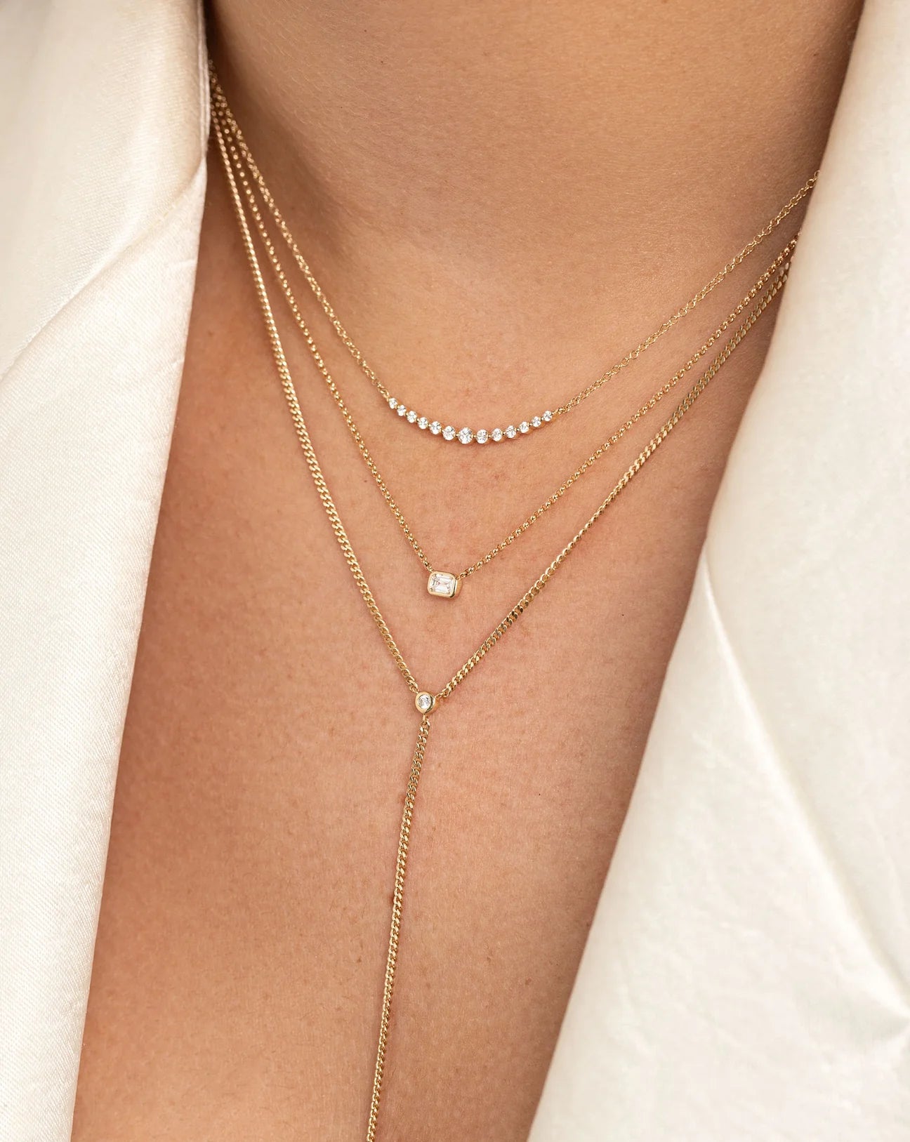 50 pointer emerald shape diamond pendant with bezel setting in a hallmark, nine carat, yellow gold chain stacked/layered with other dainty gold chains.