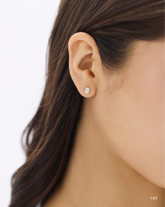 The image shows a close up of a woman wearing a one carat emerald cut lab diamond set in 14 carat hallmark white gold.