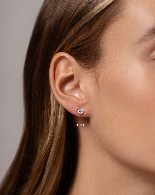 Close up of a woman wearing a one carat diamond solitaire stud earring set in 14 carat white gold.