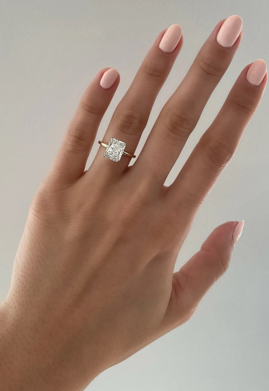 The image shows a hand wearing a 2.5 radiant cut lab diamond ring in 14 carat yellow gold band