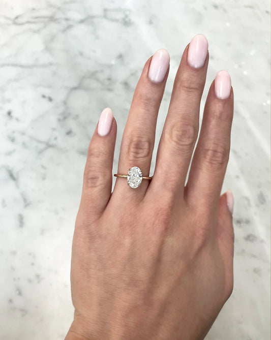 2 carat oval lab diamond solitaire ring in 14kt hallmark yellow gold band. The image showcases the ring being adorned and it’s size on a hand.