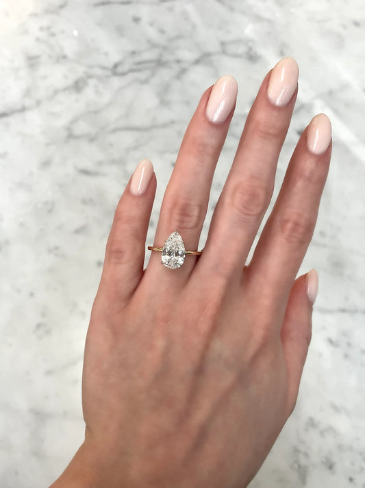 The image shows a hand wearing a 3 carat pear shape diamond in a sleek 14 carat hallmark yellow Gold band.