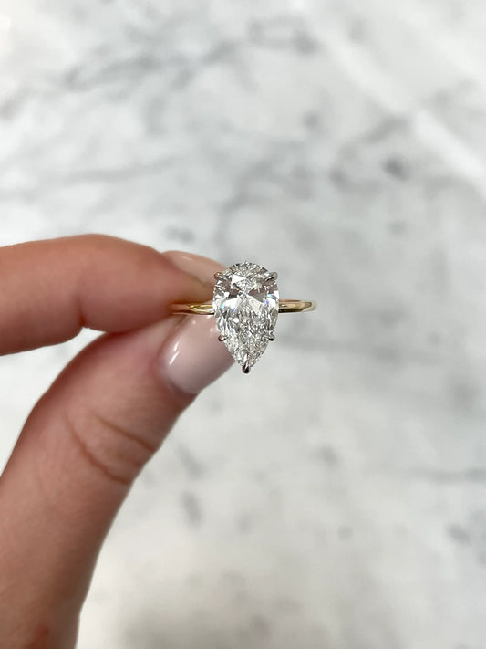The image shows a close up of a pear shape diamond in a sleek 14 karat hallmark, yellow gold band. It can be seen that the ring is held with a six prong setting, showing the cut and clarity of the diamond.