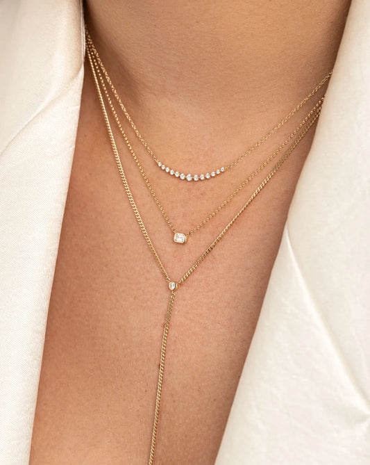 50 pointer emerald shape diamond pendant with bezel setting in a hallmark, nine carat, yellow gold chain stacked/layered with other dainty gold chains.