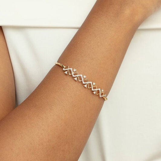 The image shows a hand wearing a bangle with geometric design in lab diamonds set on a 14kt hallmark yellow gold bangle