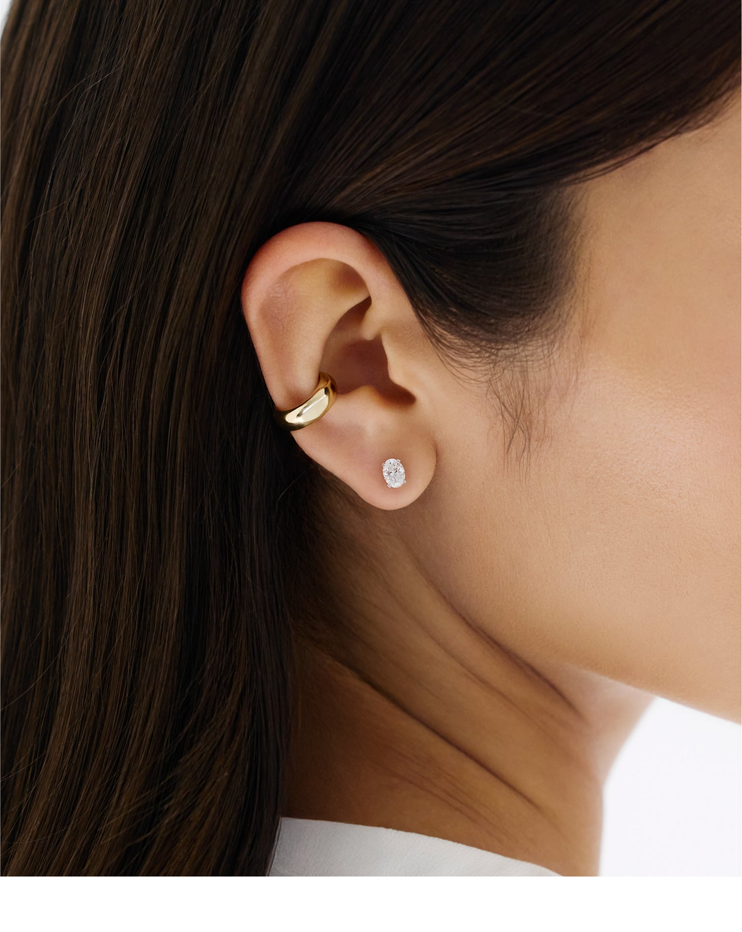 Close-up of an ear wearing a gold hoop earring and an oval diamond stud earring.