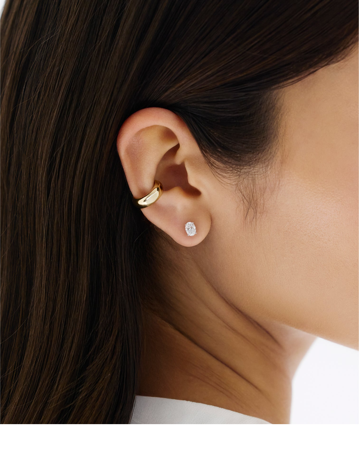 Close-up of an ear wearing a gold hoop earring and an oval diamond stud earring.